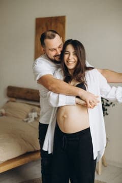Expecting parents laughing together, arms wrapped around the baby bump