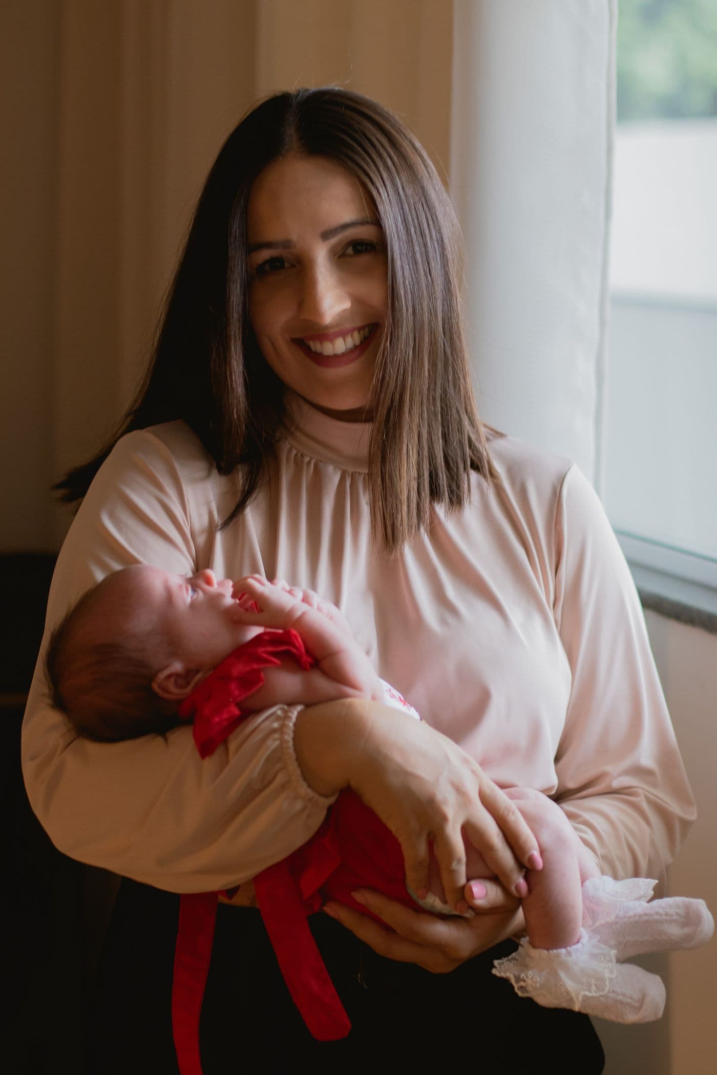 A smiling mother holding her newborn in soft window light