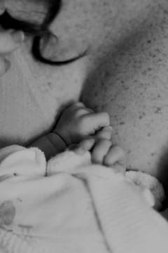 A newborn's tiny hands resting against a parent, in soft black and white